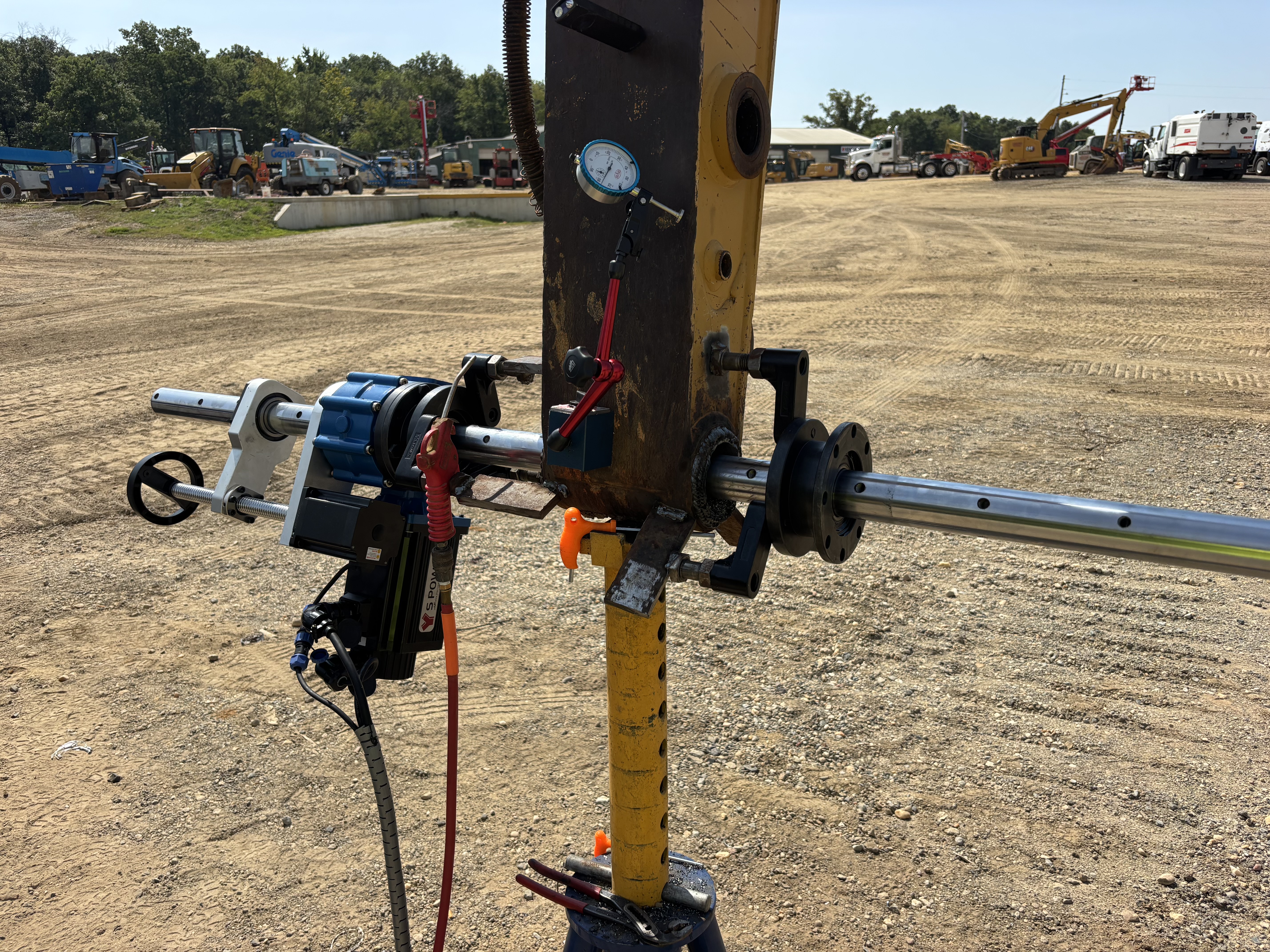 Portable line boring machine with gauges and motor mounted on heavy equipment in a dirt yard.